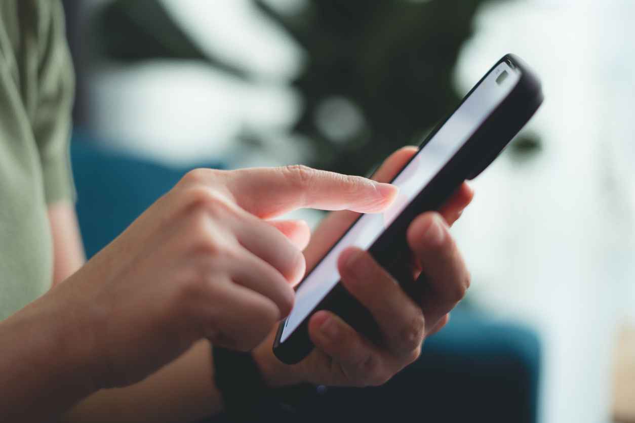 Close-up shot of female hands using smart phone for searching shopping online or surfing social media, sitting on sofa in living room at home.