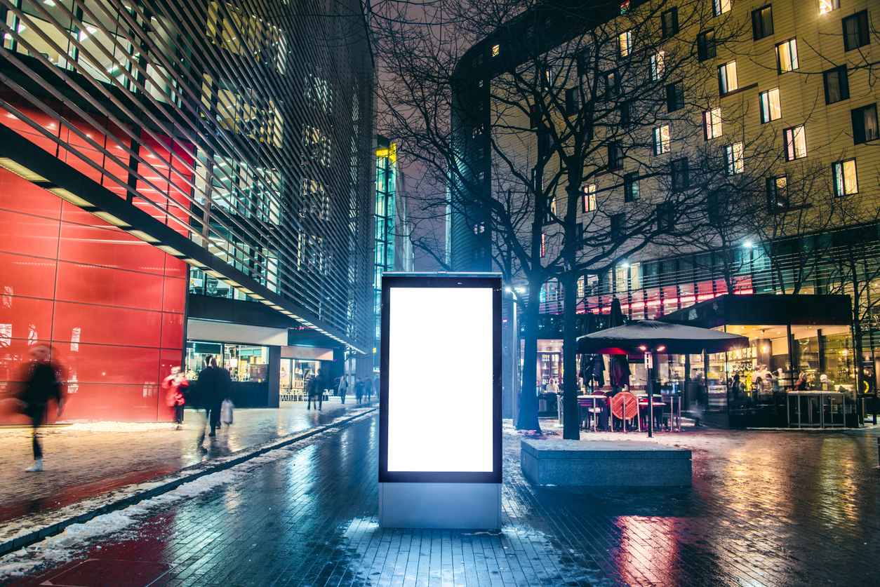 An illuminated blank display screen on a busy street at night