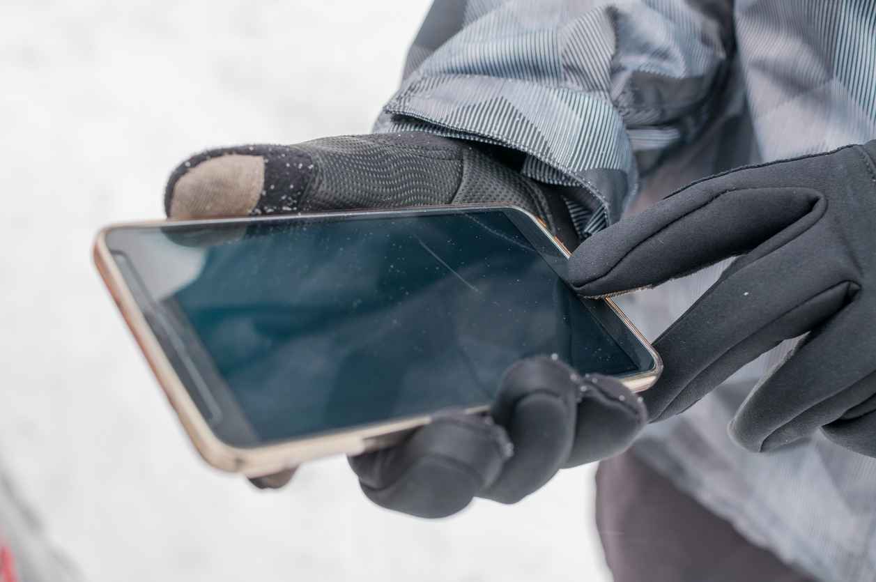 Closeup of man using smart phone in winter with winter gloves for touch screens