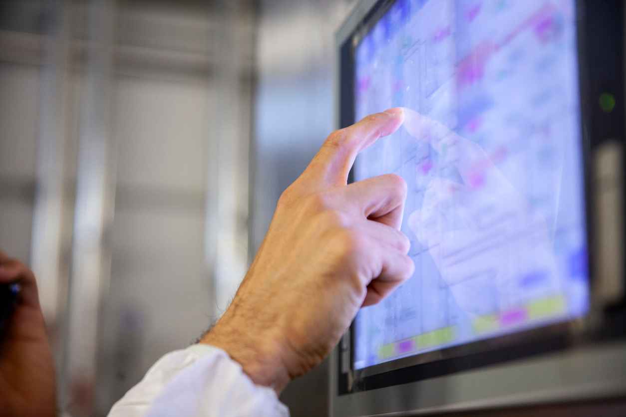 Close-up shot of a factory worker's hand pointing at a computer screen