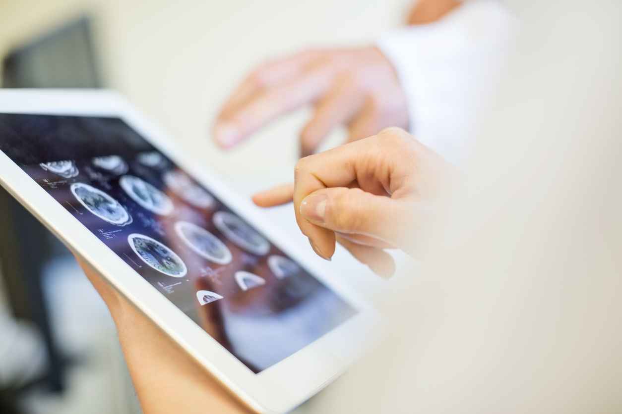 Close up of doctors hands pointing at brain xrays images on digital tablet. Medical team in clinic analyzing MRI scans on digital tablet.