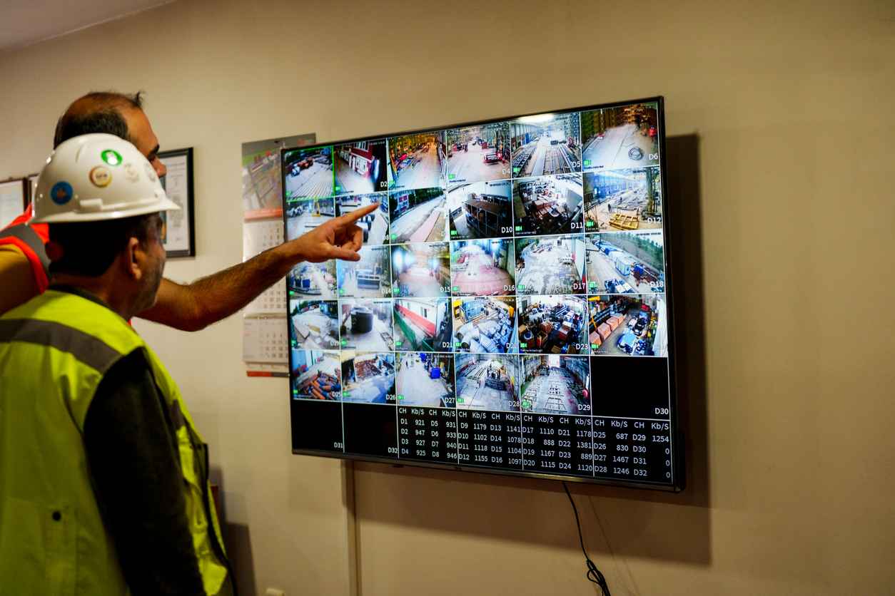 mature men discussing surveillance footages on huge screen while male operator using computer during work in security center