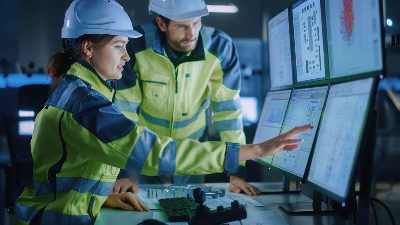 Modern Factory: Project Engineer Talks to Female Operator who Controls Facility Production Line, Uses Computer with Screens Showing AI, Machine Learning Enhanced Assembly Process