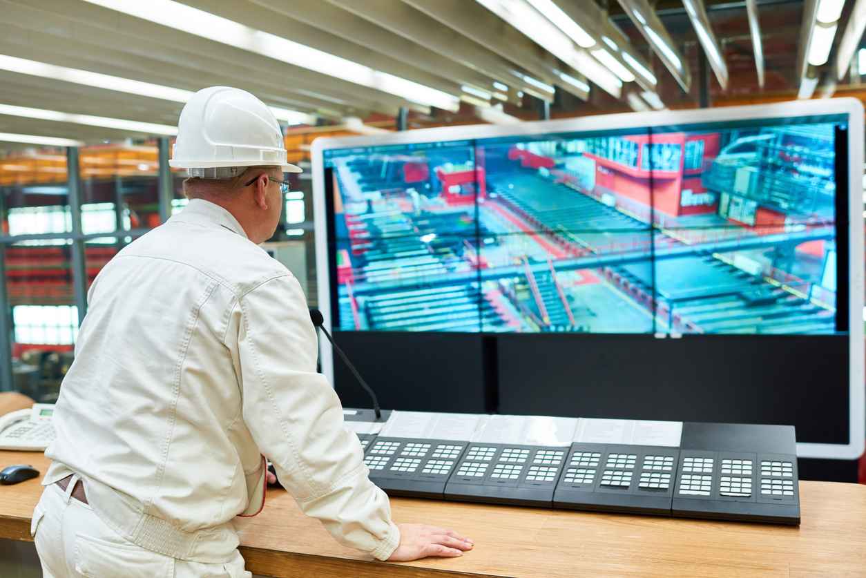 Rear view of busy stationary engineer in uniform observing working factory shop and keeping order from control room